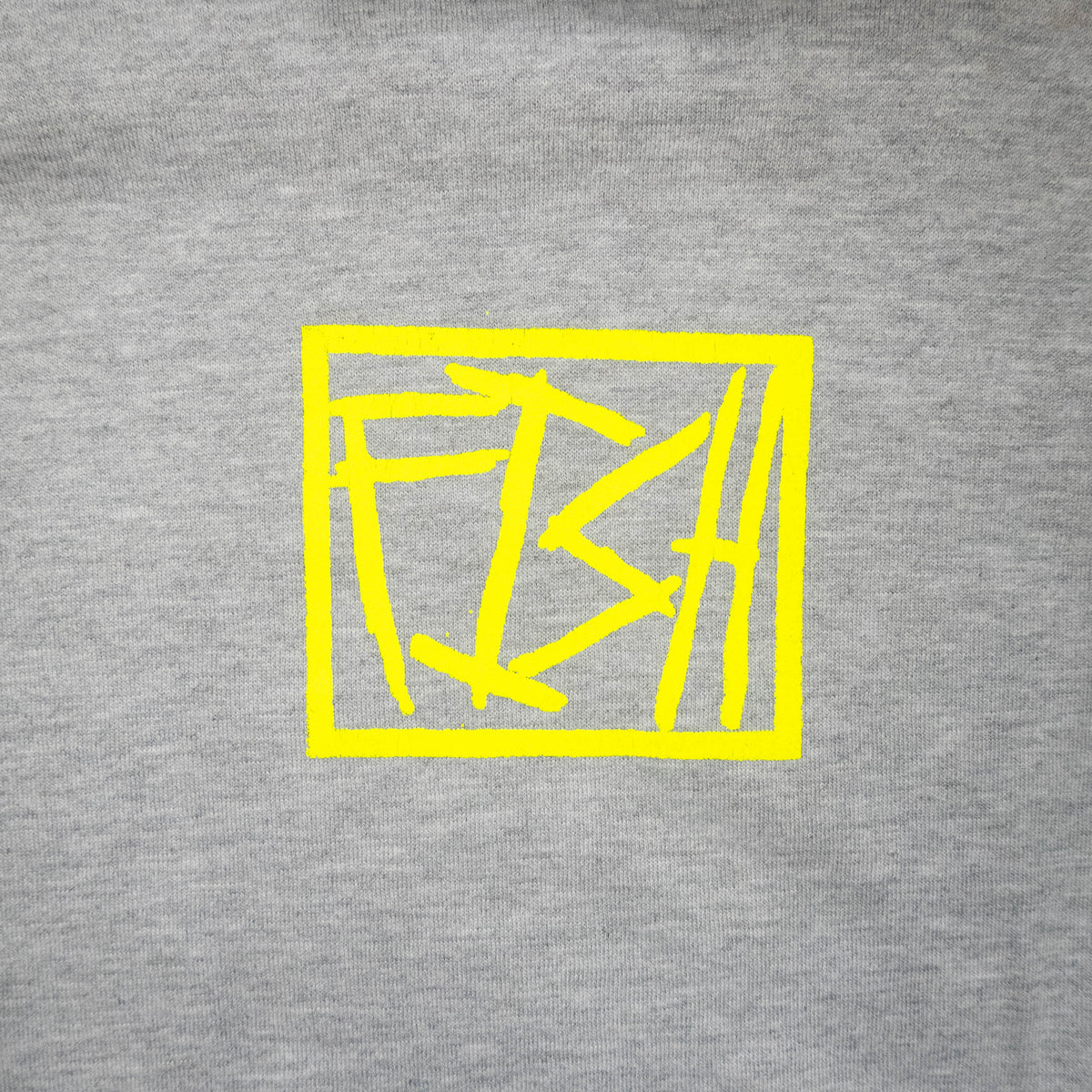 A close-up of a heather gray fabric surface with a bright yellow abstract geometric square graphic printed in the center.