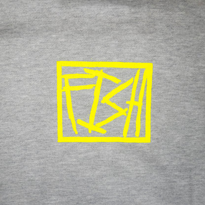 A close-up of a heather gray fabric surface with a bright yellow abstract geometric square graphic printed in the center.